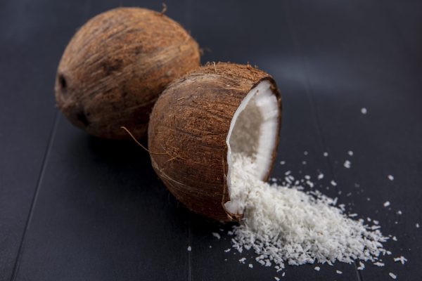 side view of fresh and brown coconuts with coconut powder on a black background